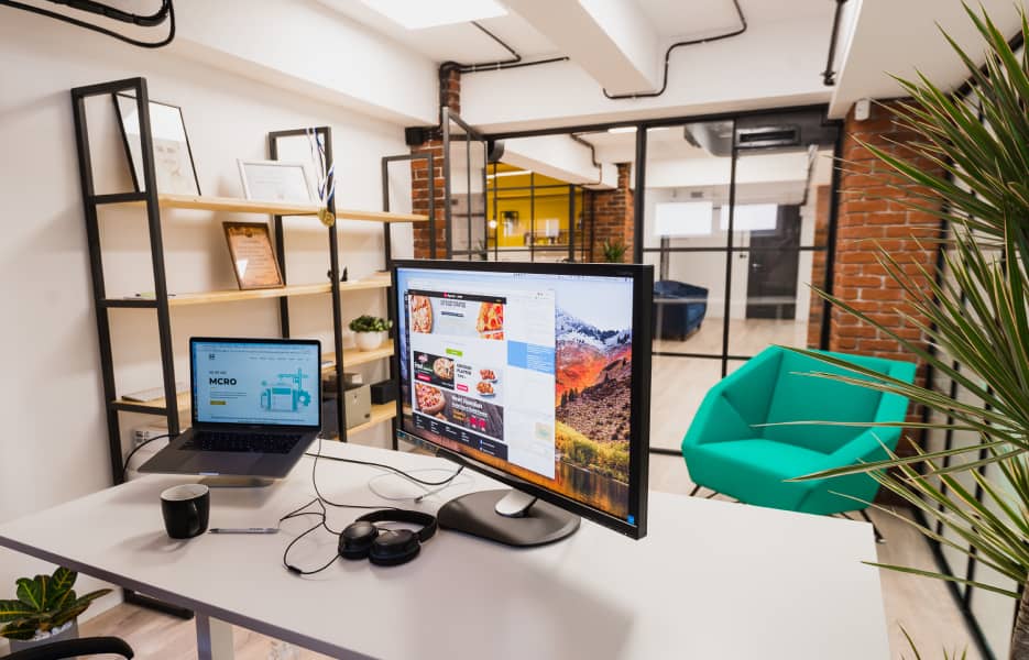 Turned on monitor and silver laptop on a white desk inside an office Turned on monitor and silver laptop on a white desk inside an office
